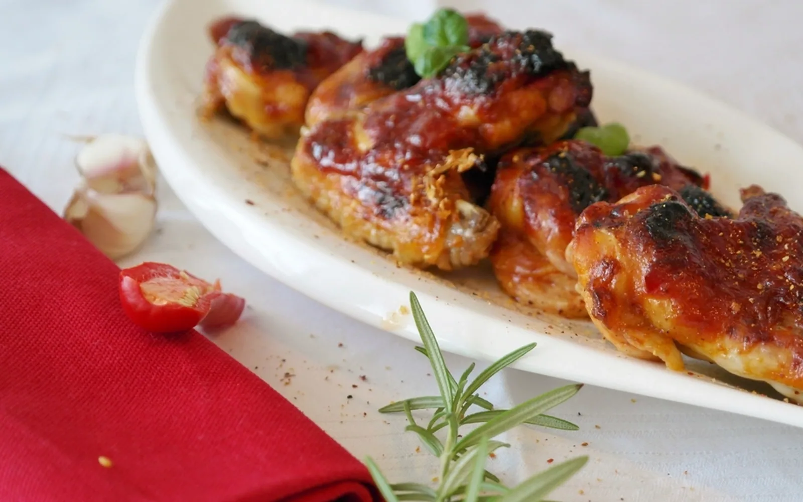 Glazed chicken wings on a white serving plate with rosemary