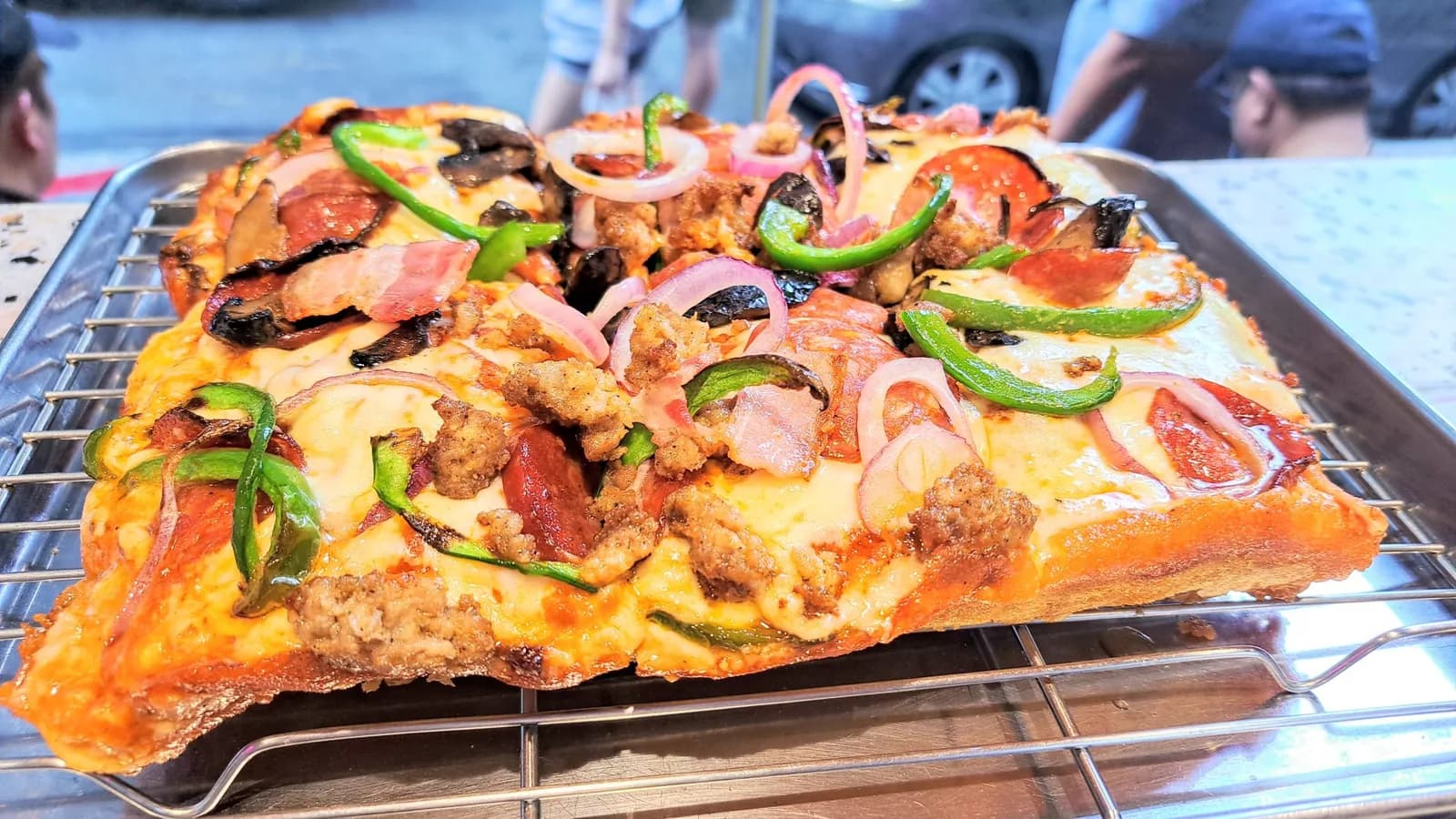Rectangular pizza loaded with peppers, onion and meat on a cooling rack